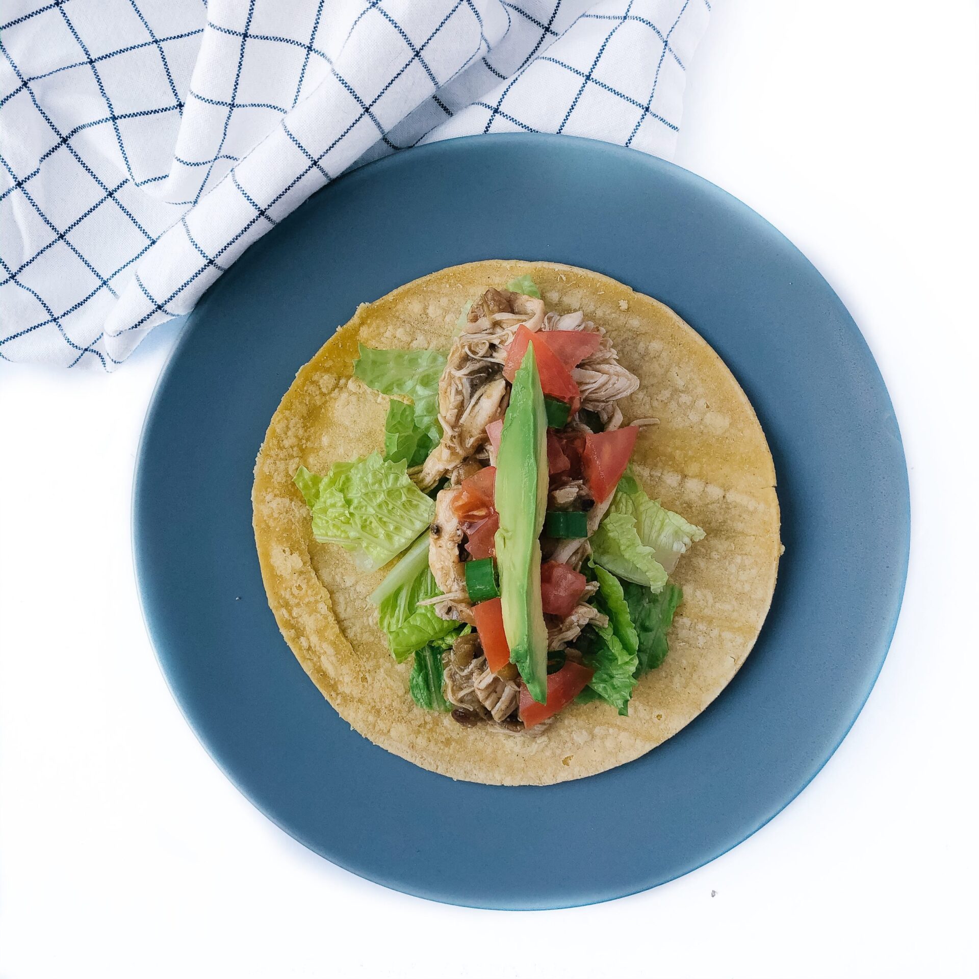 chicken and lentil tacos assembled on a blue plate with lettuce, tomato, avocado topping