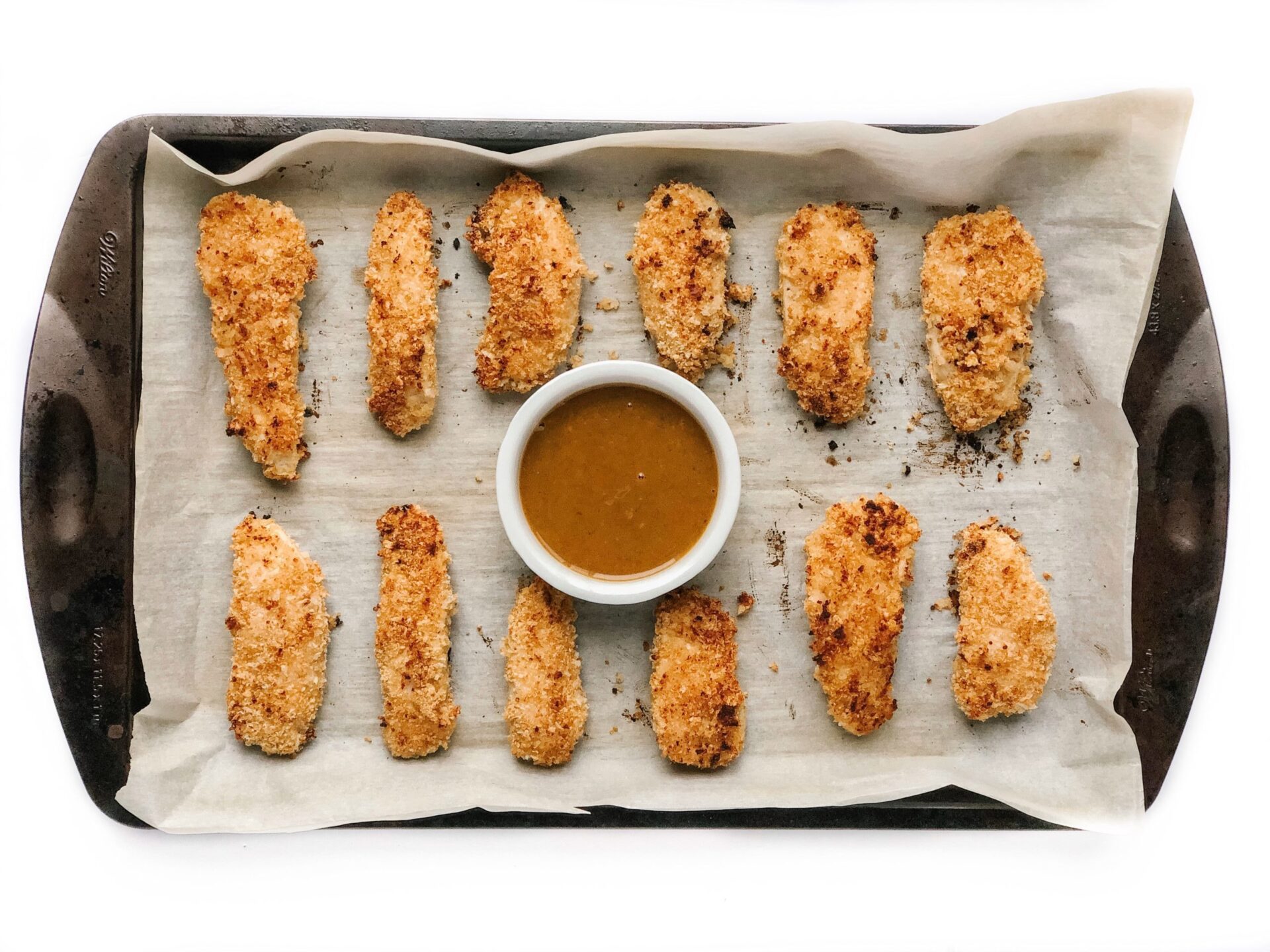 quinoa chicken strips with dipping sauce on a sheet pan